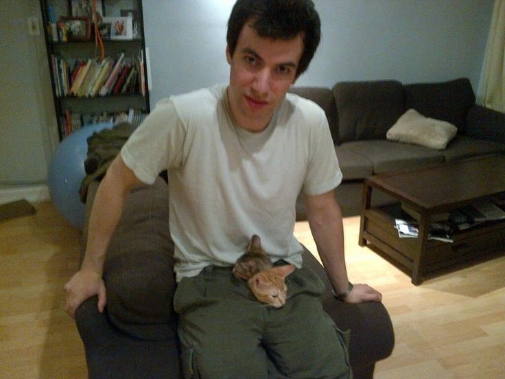 a man is sitting on a couch with a cat in his lap and looking at the camera