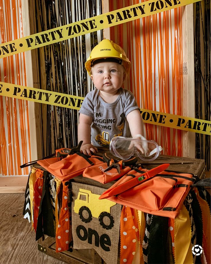 a baby wearing a hard hat sitting on top of a table with caution tape around it