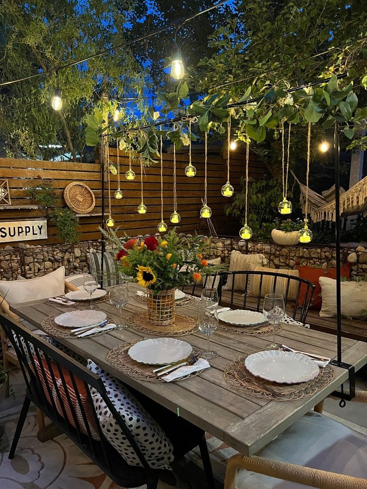 a table with plates and place settings on it in a garden setting at night time