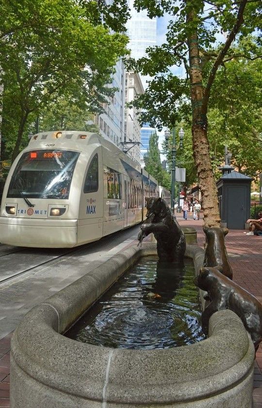 a public transit train on the tracks next to a fountain with water running through it