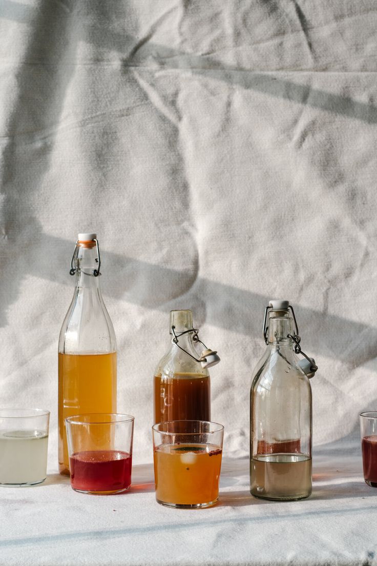 four different types of liquid in glass bottles and shot glasses on a white table cloth