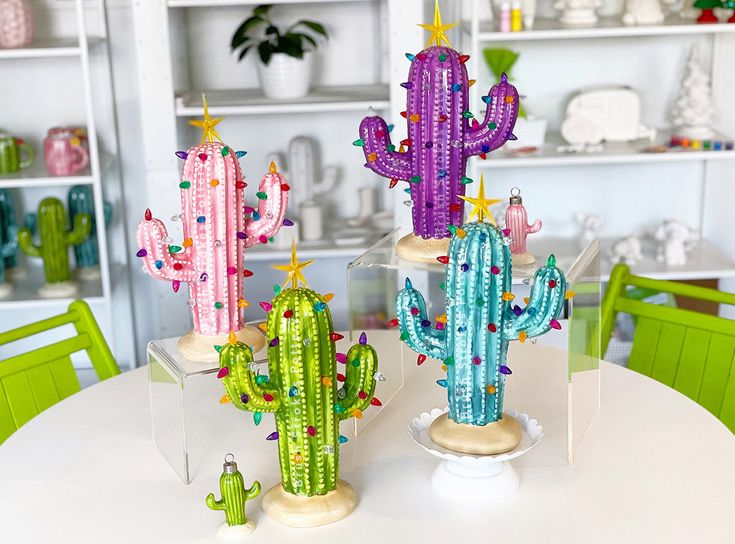 three colorful cactus decorations sitting on top of a white dining room table with green chairs