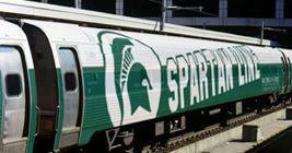 a green and white train is on the tracks near a building that has an advertisement on it