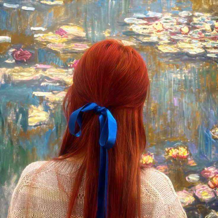 a woman with long red hair wearing a blue bow in front of a painting that has water lilies on it