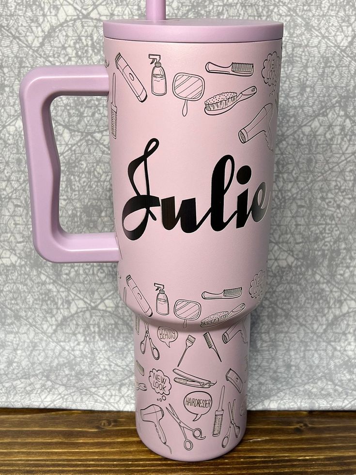 a pink travel mug with the word sullie on it and various items around it