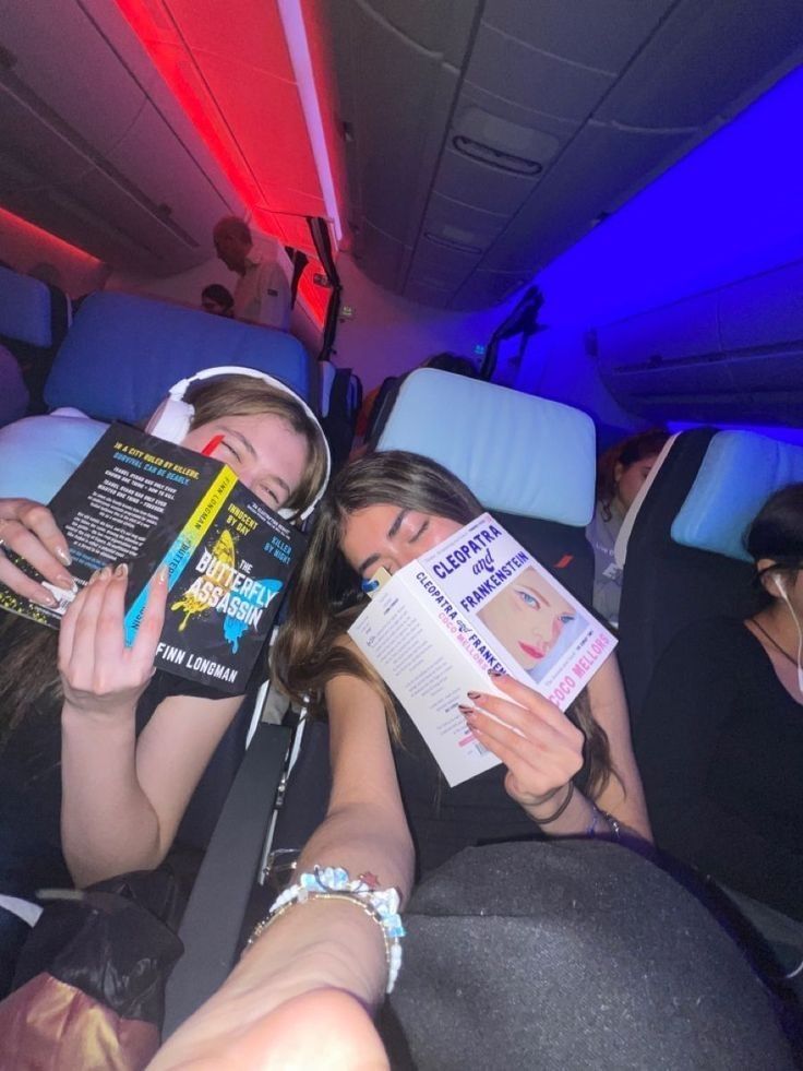 two girls are sleeping on an airplane reading books