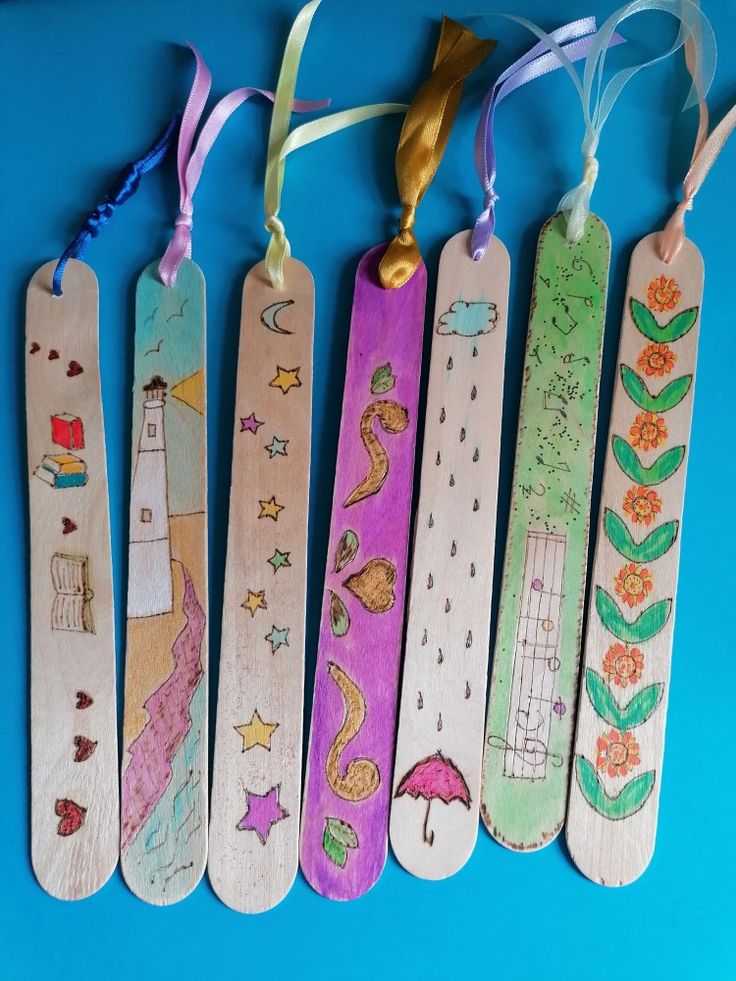 five wooden bookmarks with designs on them hanging from ribbons and tags attached to strings