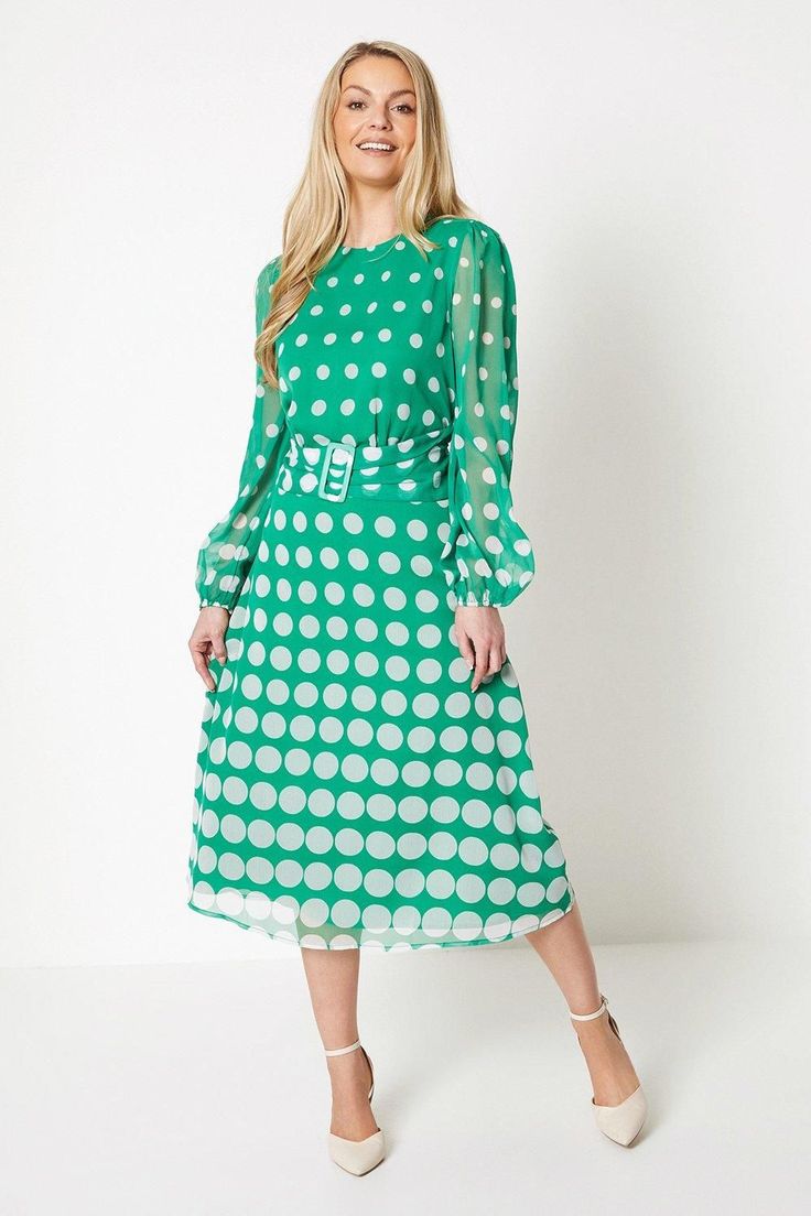 a woman wearing a green polka dot dress with long sleeves and a belted waist