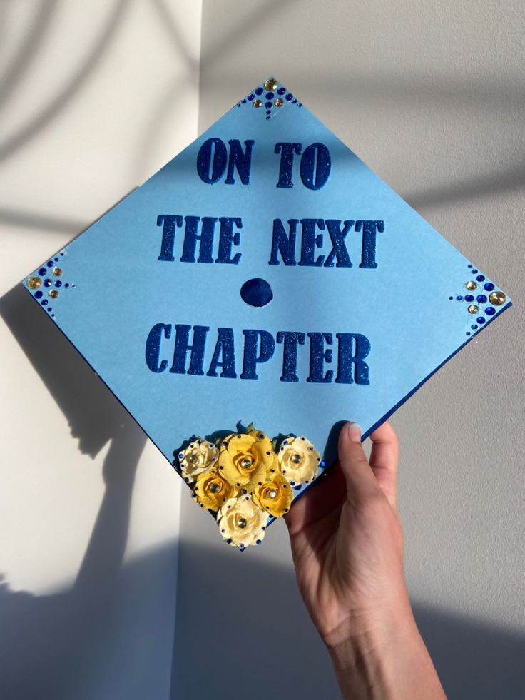 a blue graduation cap with the words on to the next charter written in gold flowers