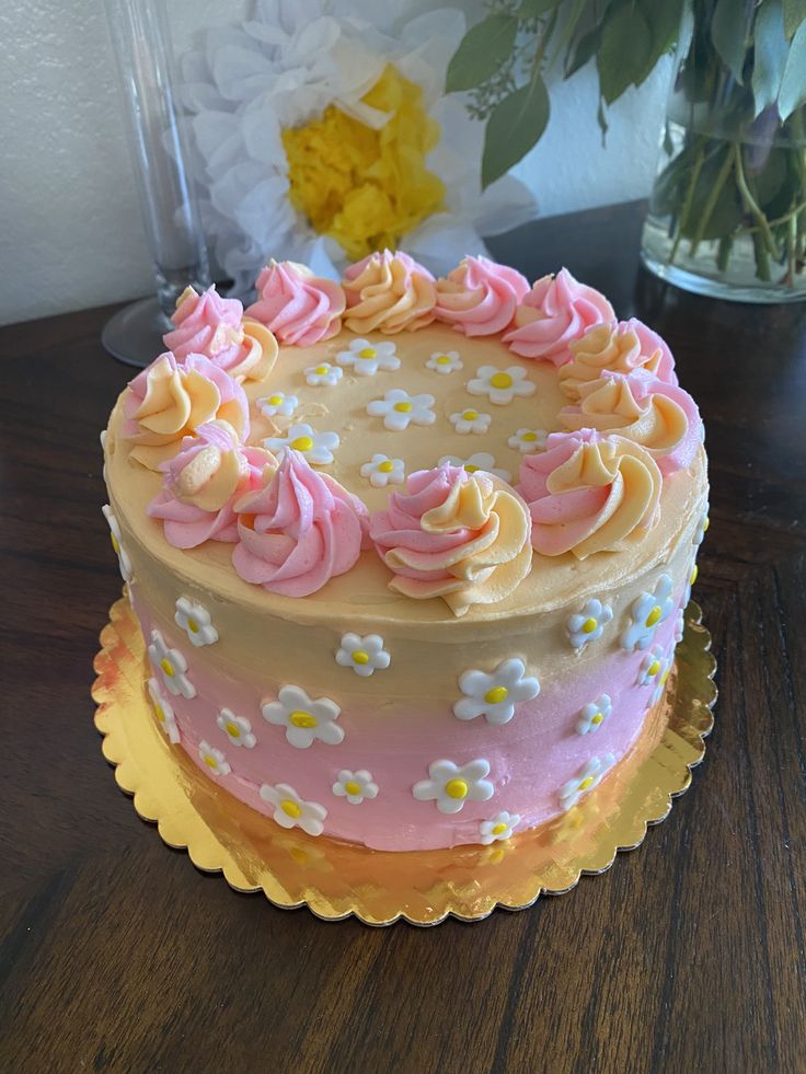 a pink and yellow cake sitting on top of a wooden table next to a vase with flowers