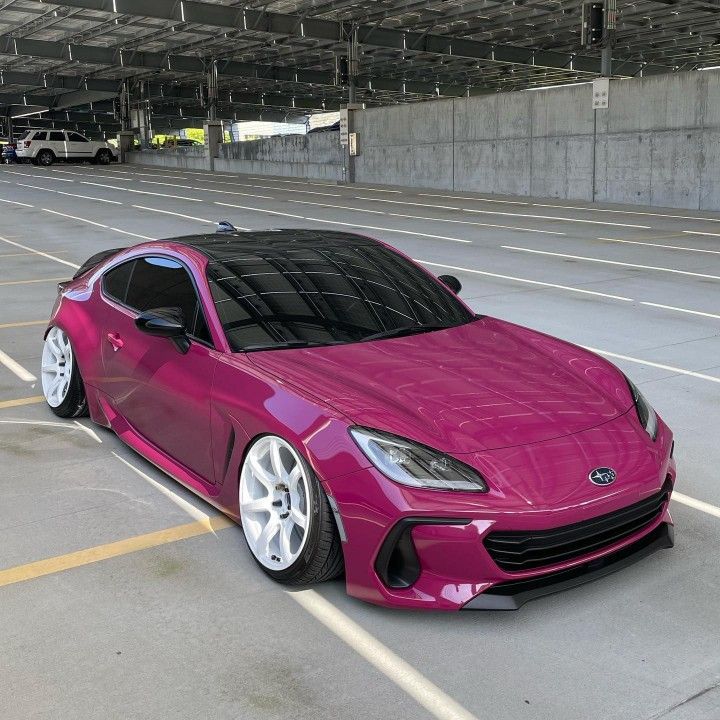 a pink sports car parked in an empty parking lot next to some concrete walls and yellow lines