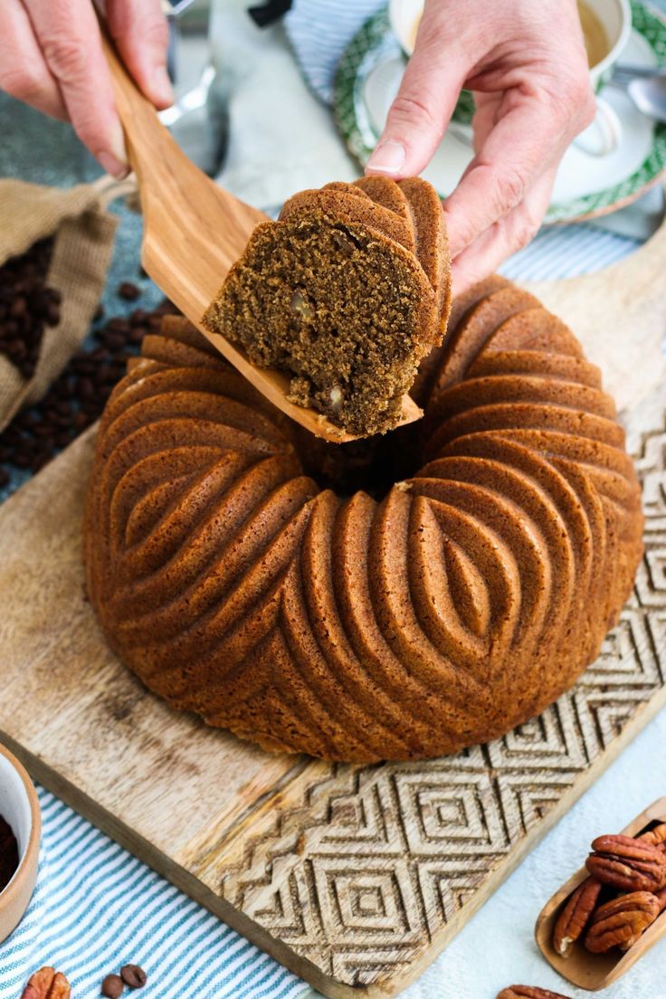 a person holding a wooden spoon over a bundt cake on a cutting board with pecans around it