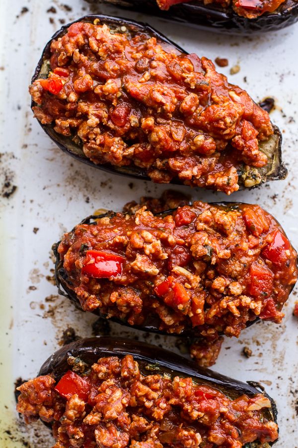 three stuffed eggplant halves on a baking sheet covered in sauce and ground meat