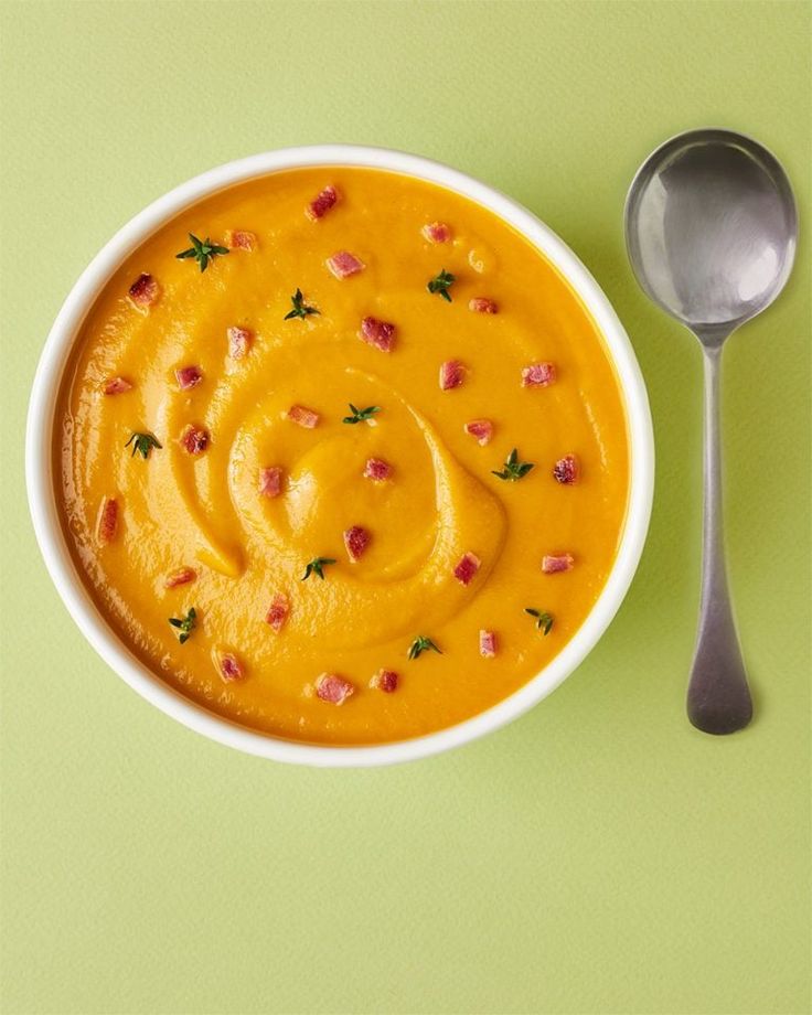 a white bowl filled with soup next to a spoon on a green tablecloth covered surface