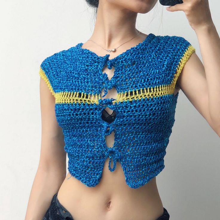 a woman wearing a blue crocheted crop top talking on a cell phone with her hands in her pockets