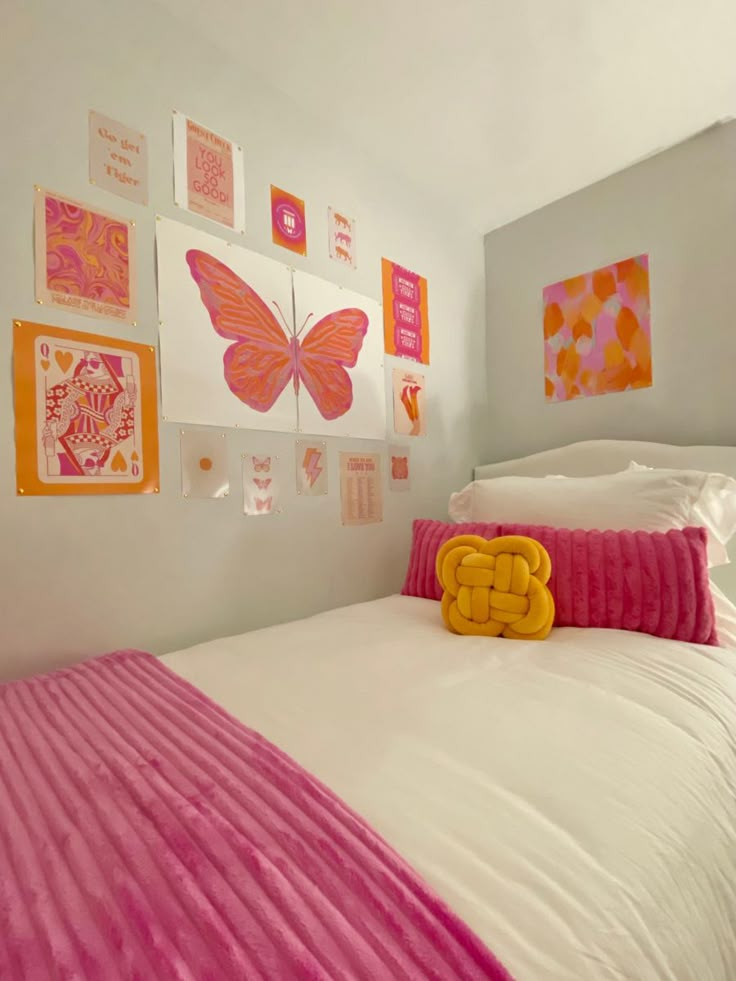 a white bed topped with pink and yellow pillows next to a wall covered in pictures