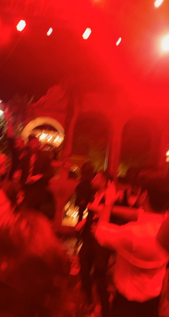 blurry photograph of people dancing in a red lit room with lights on the ceiling