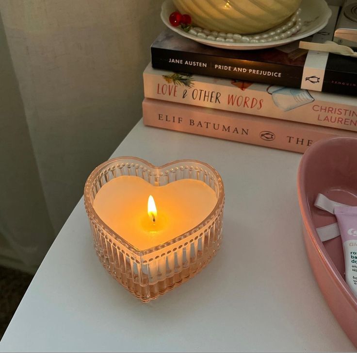 a heart shaped candle sitting on top of a table next to books and a bowl