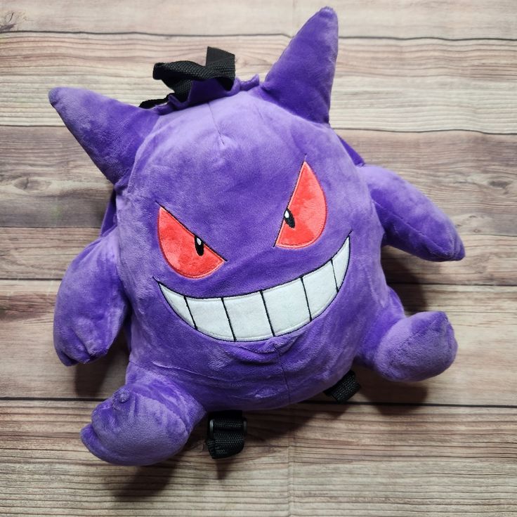 a purple stuffed animal with big red eyes and fangs on it's face sitting on a wooden floor