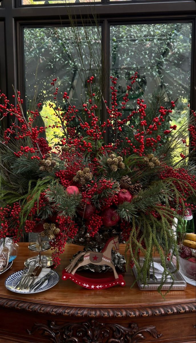 a vase filled with red flowers on top of a wooden table next to a window