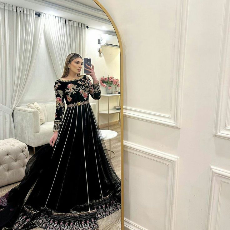 a woman taking a selfie in front of a mirror wearing a black and gold gown