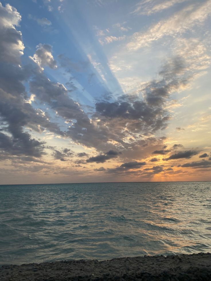 the sun is setting over the ocean with some clouds in the sky and water below