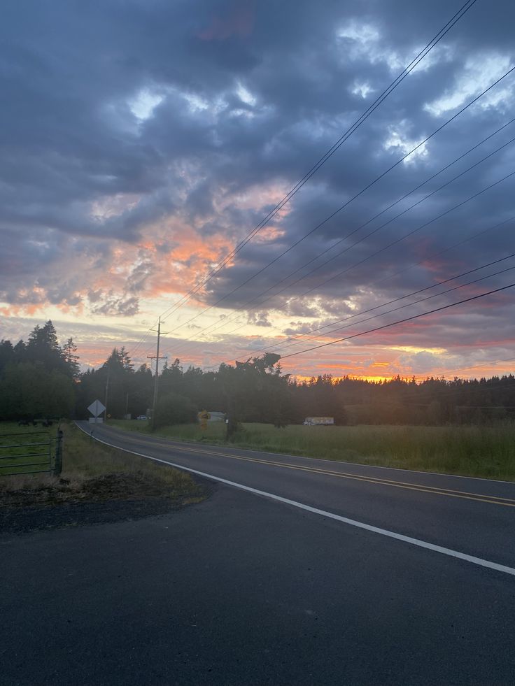 the sun is setting on an empty road with power lines in the foreground and trees to the side