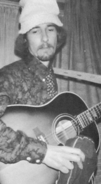 an old photo of a man holding a guitar and wearing a beanie on his head