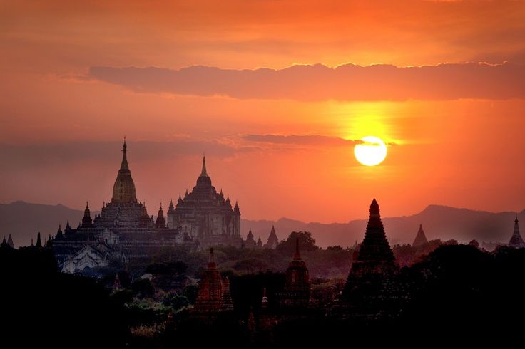 the sun is setting over an ancient city with spires and buildings in silhouette,