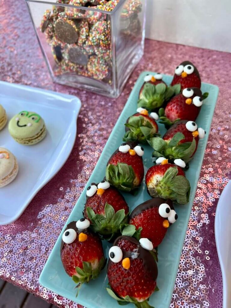 some strawberries with googly eyes are on a blue plate next to other desserts