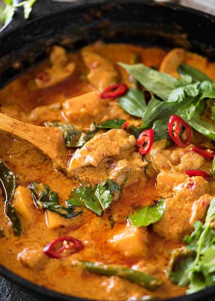 a skillet filled with chicken and vegetables on top of a wooden spatula next to a green leafy garnish