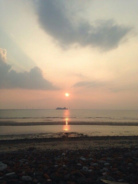 the sun is setting over the ocean with rocks on the shore