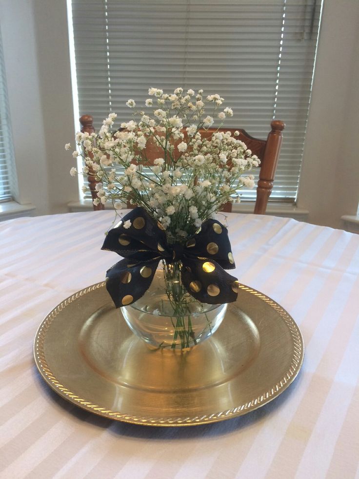 a vase filled with white flowers on top of a gold plate covered in black ribbon