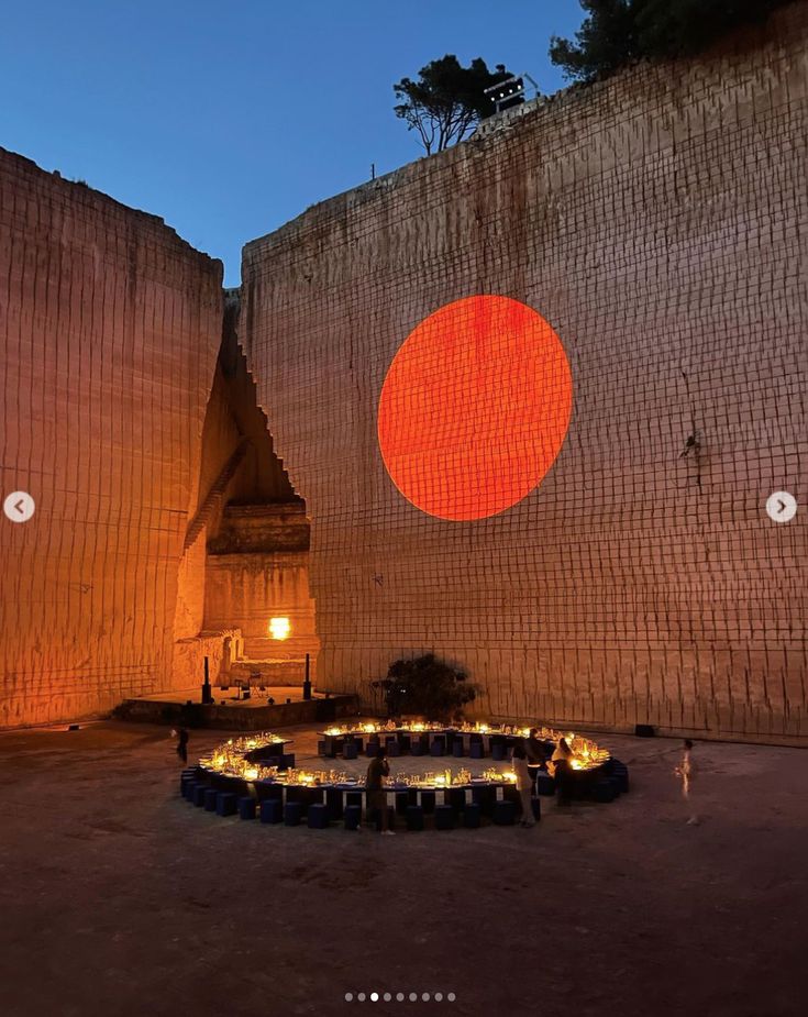 an outdoor dining area is lit up at night with orange and red circles on the wall