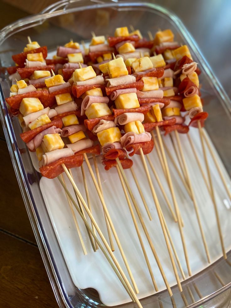 several skewered food items on sticks in a clear container with white cloth underneath