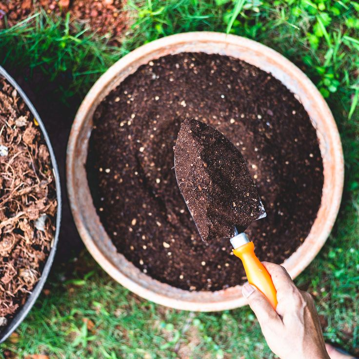 a person is holding a shovel and digging dirt into a potted plant in the grass