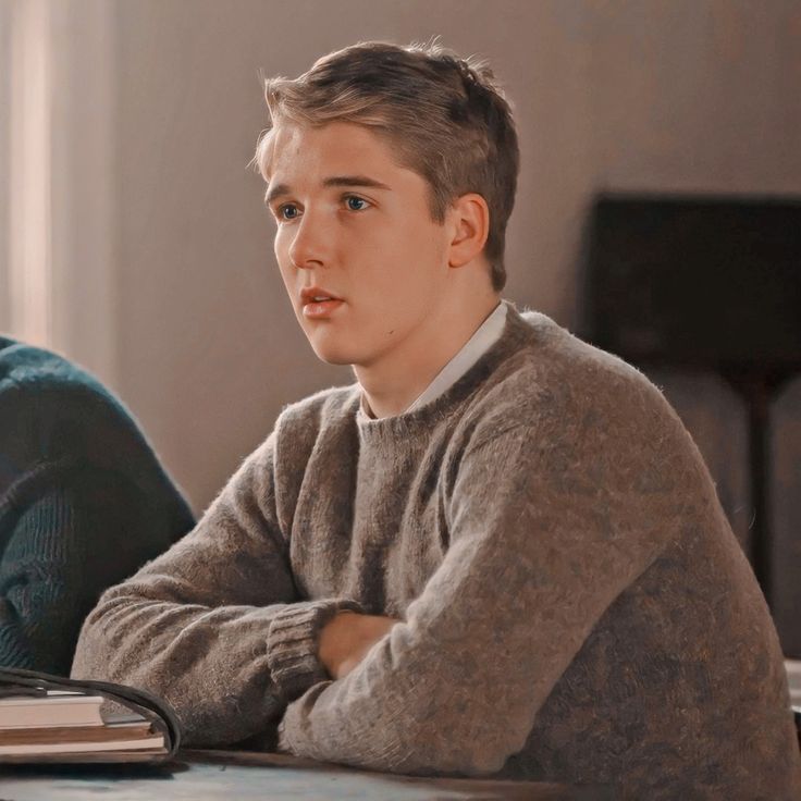 a young man sitting at a table in front of a laptop computer with his arms crossed