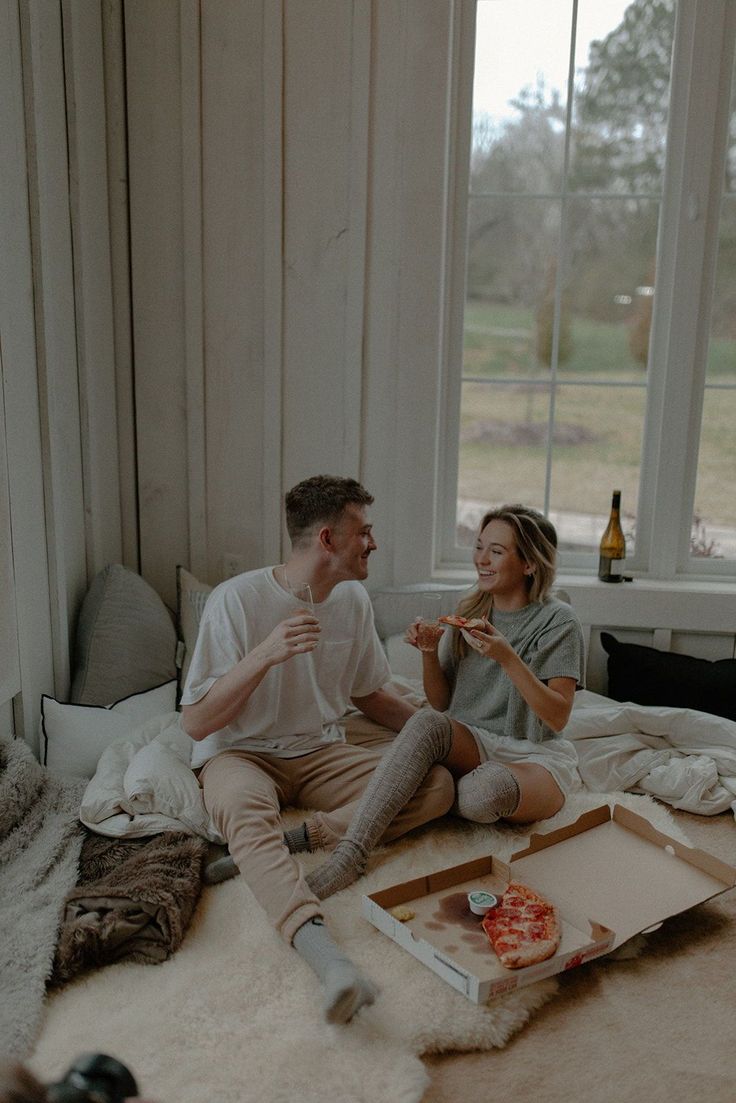 two people sitting on a bed eating pizza