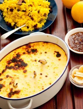 an oval casserole dish on a wooden table next to bowls of rice and oranges