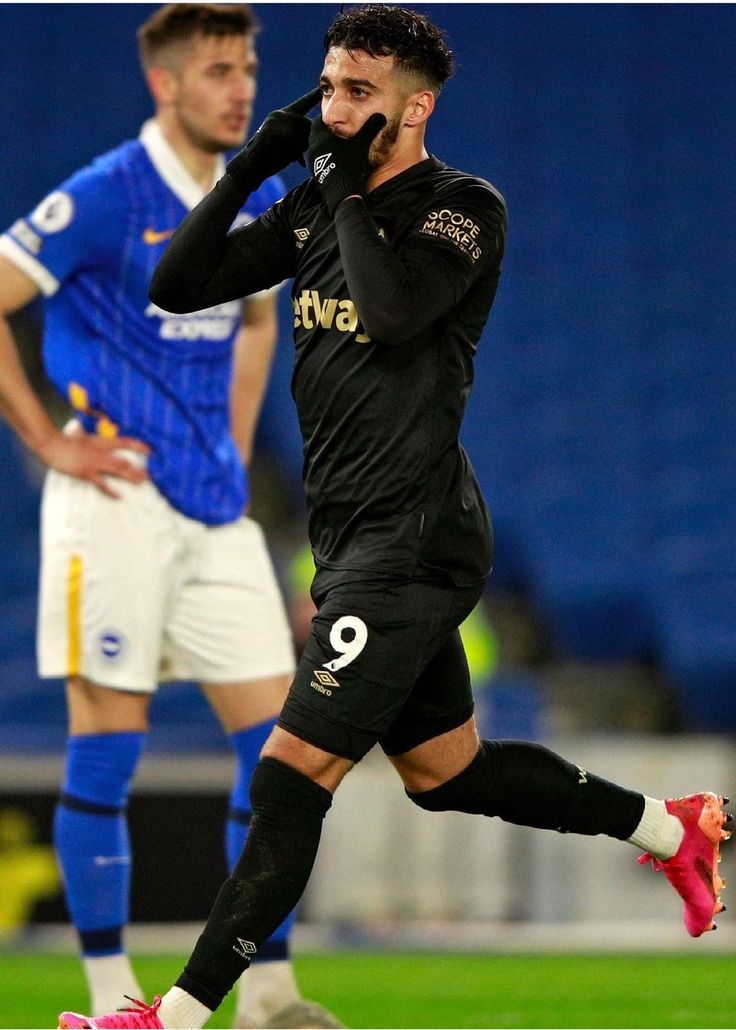 a soccer player is running on the field with his hand to his ear and talking on the phone