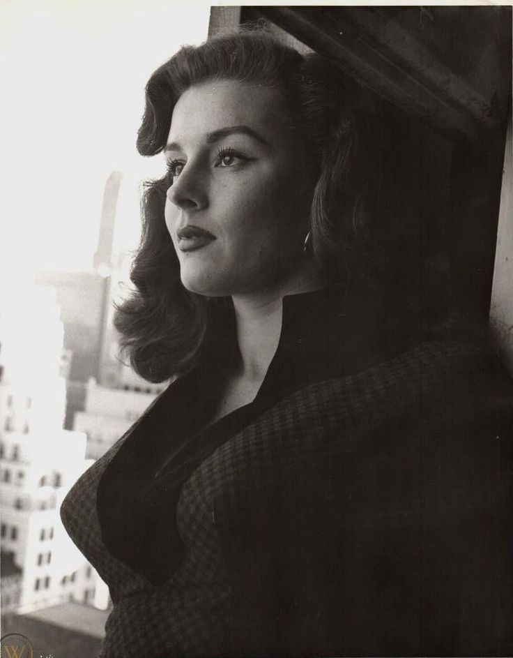 an old black and white photo of a woman looking off into the distance with buildings in the background