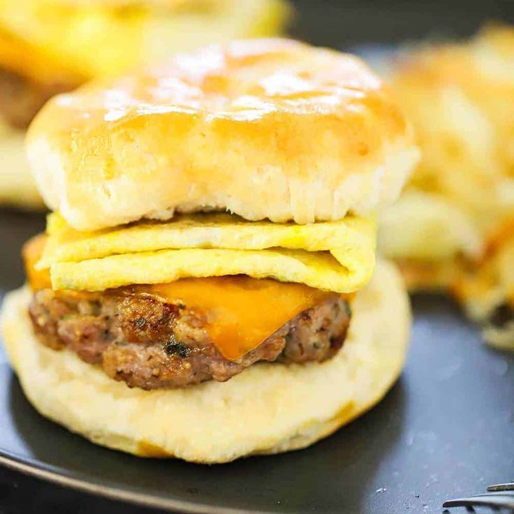 an egg and cheese breakfast sandwich is on a black plate next to some other food items