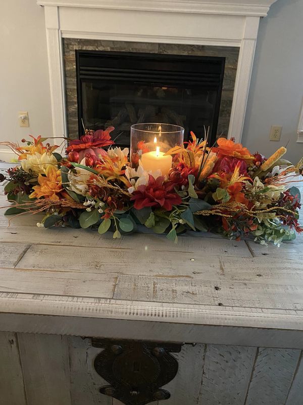 a candle is lit on top of a table with flowers and leaves in front of a fireplace