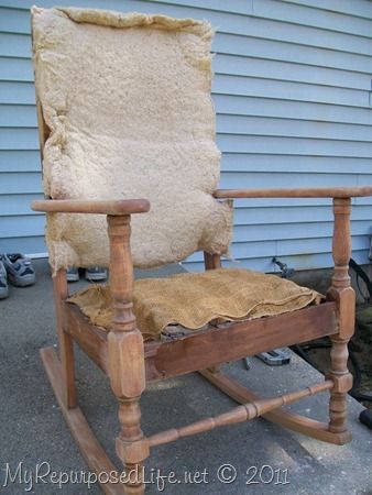 an old wooden rocking chair with a blanket on it's back and seat cushion