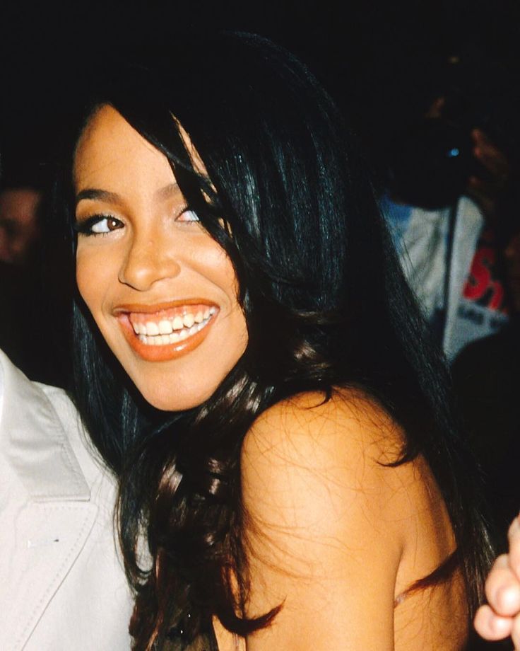 a woman with long black hair smiling at the camera while standing next to a man