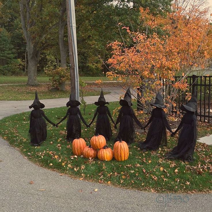 halloween decorations in the shape of witches holding hands and pumpkins on grass near fence