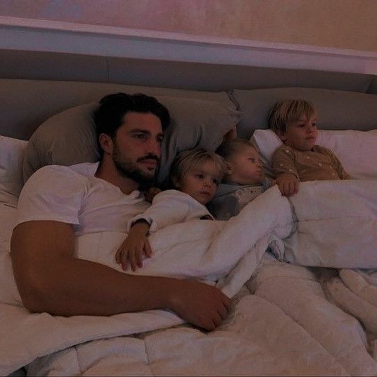 a man laying in bed with two children and an adult looking at the camera while he sleeps