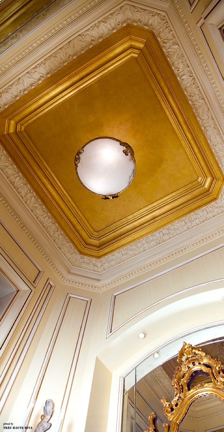 an ornate gold ceiling light fixture in a room with white paneled walls and ceilings