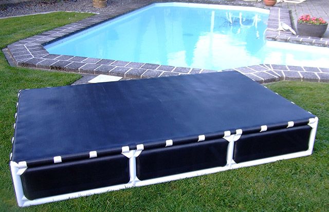 an empty swimming pool in the grass next to a brick patio with a blue cover over it