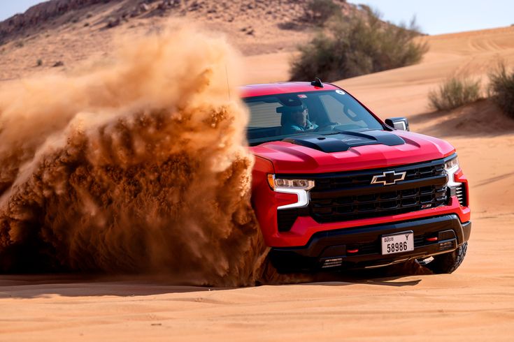 a red truck driving through the desert with sand blowing up from it's tires